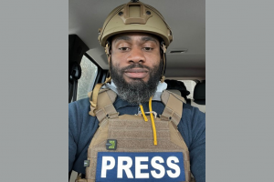 Man wearing body armor that has the word "Press" stamped across the front.