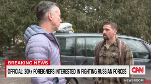 Journalist in winter jacket interviewing man in plaid shirt. CNN Logo in corner. Chyron reads: Official, more than twenty thousand foreigners interested in fighting Russian forces.